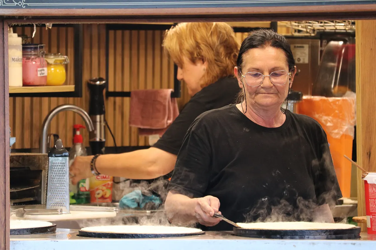A vendor cooking pancakes at an outdoor stall while customers wait
