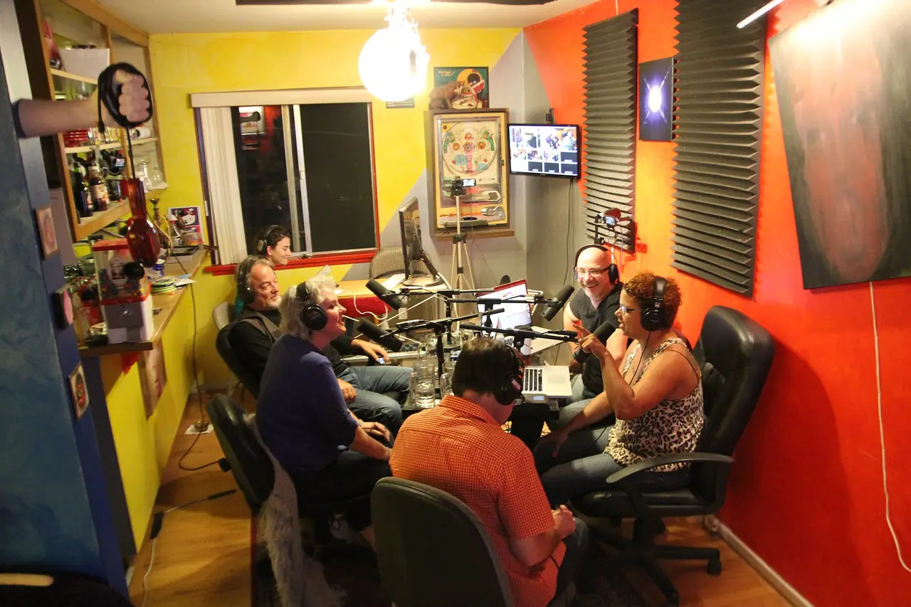 A podcast host and guests talking around microphones in a colourful studio