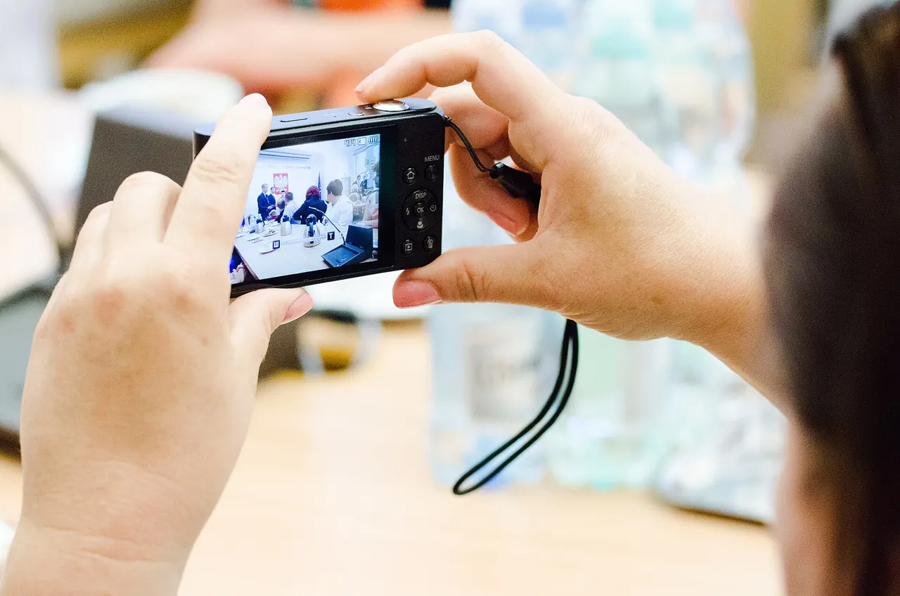 Close-up of two hands holding a compact camera, filming a meeting on its screen