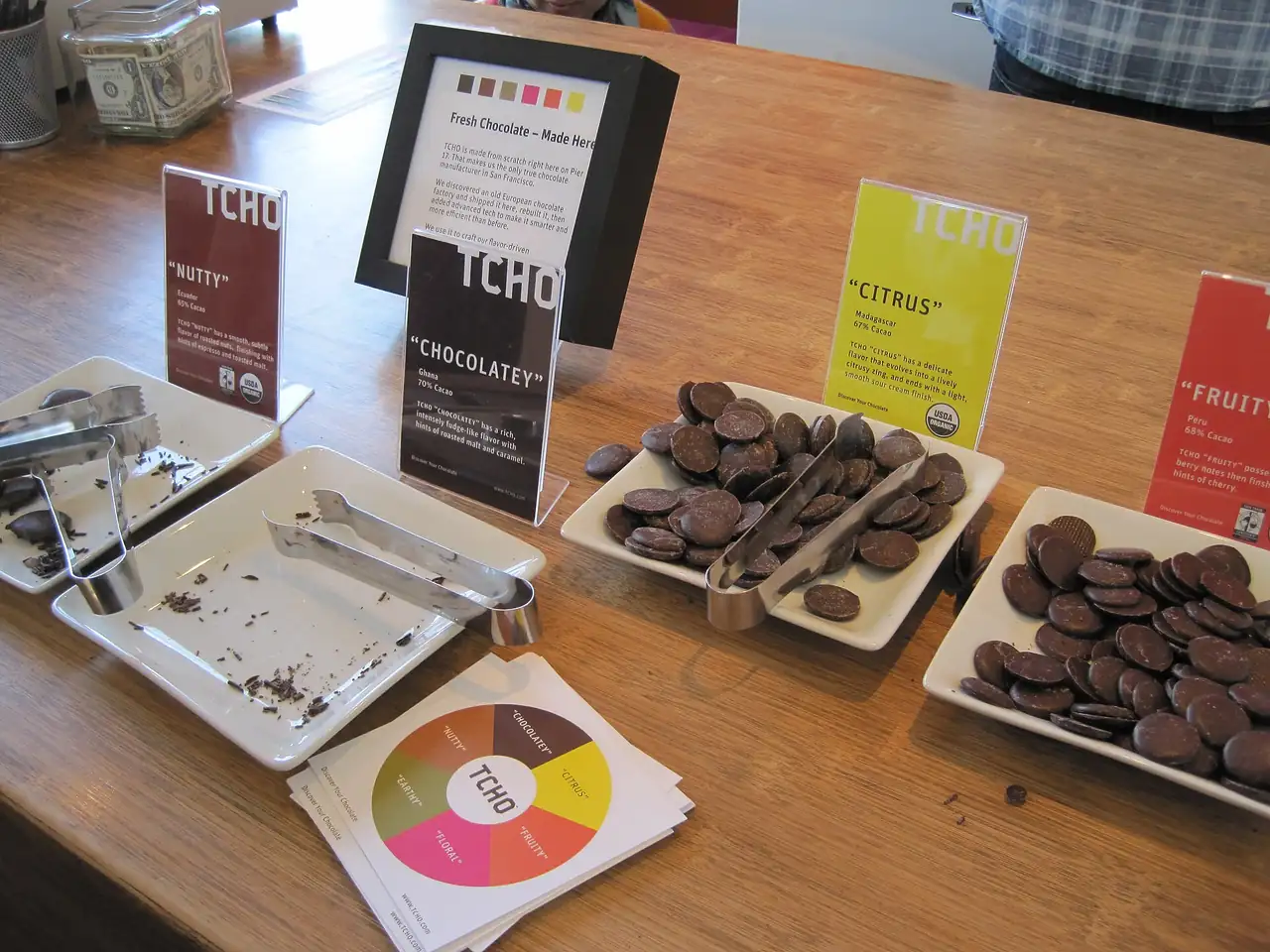 A wooden table with trays of free chocolate samples and small tasting cards
