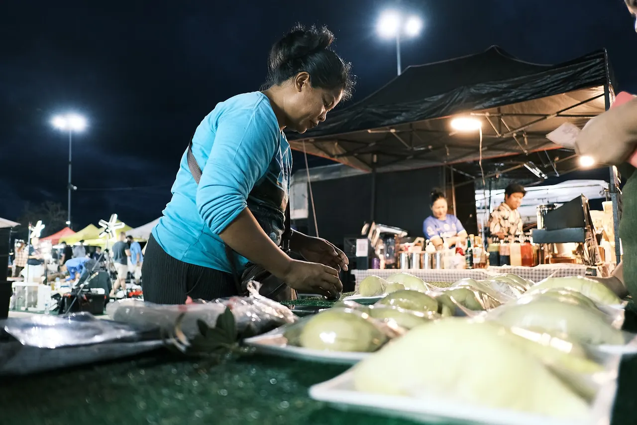 A vendor arranging fresh fruit on a night-market stall under bright lights