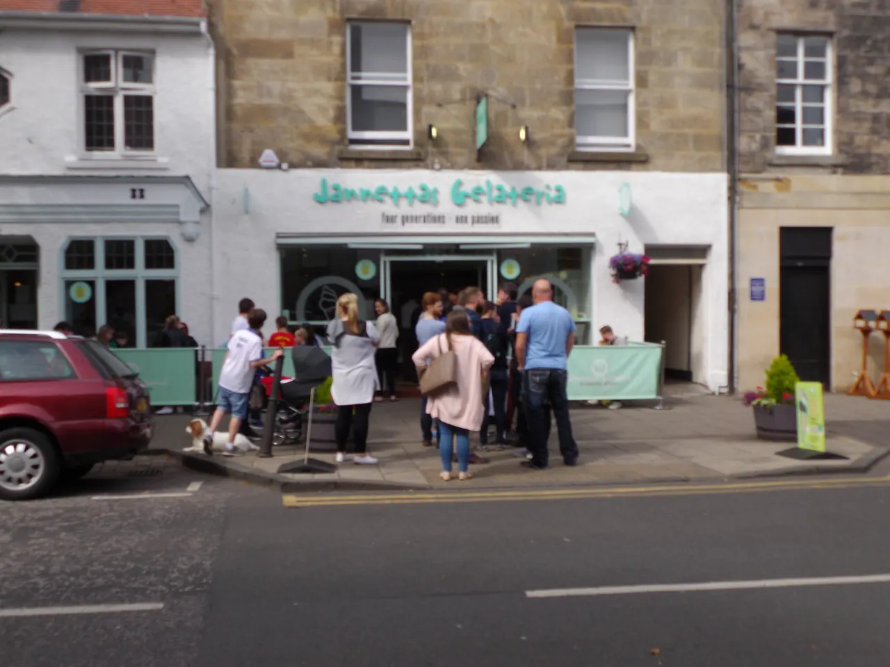 People queuing outside an ice-cream shop on a sunny street